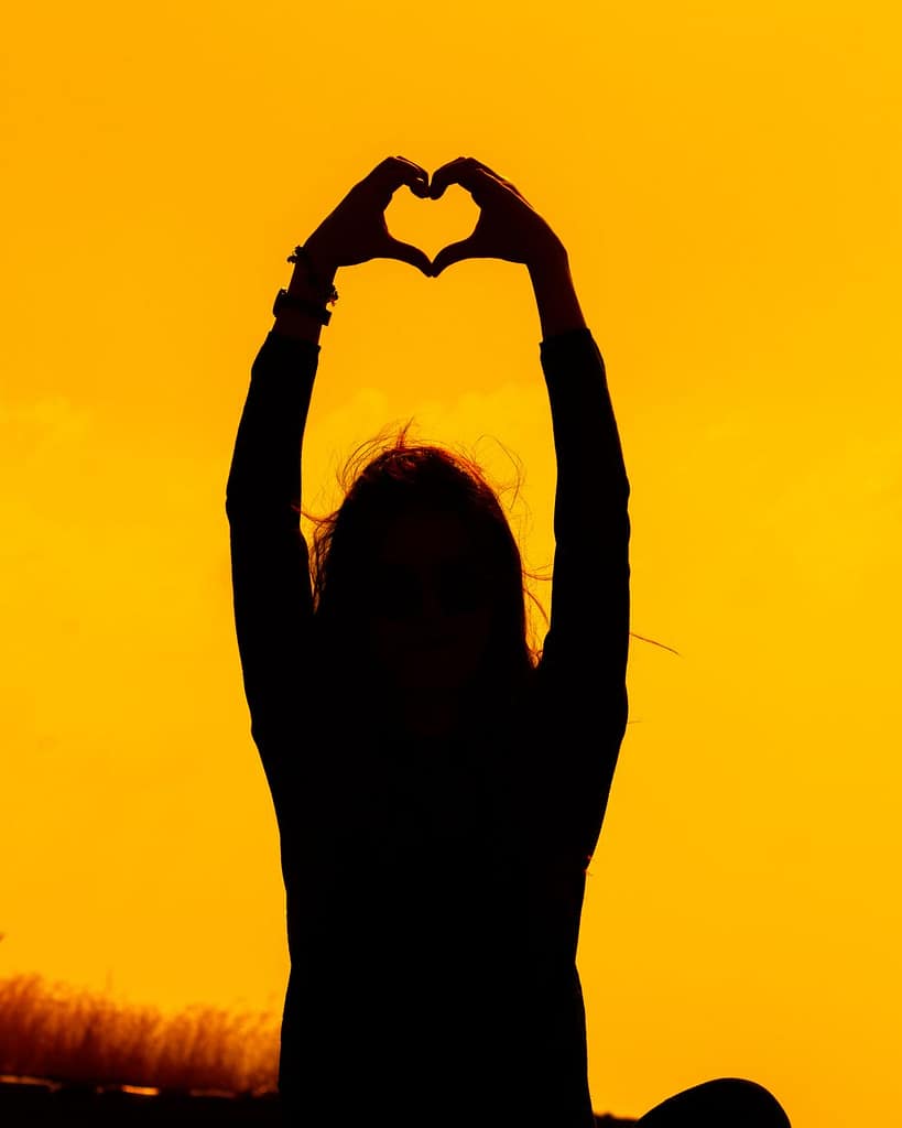 silhouette of person making heart gesture at sunset